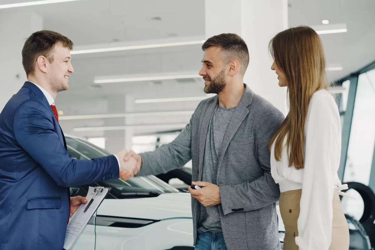 A salesperson shaking hands with a customer while his partner looks on in a dealership showroom