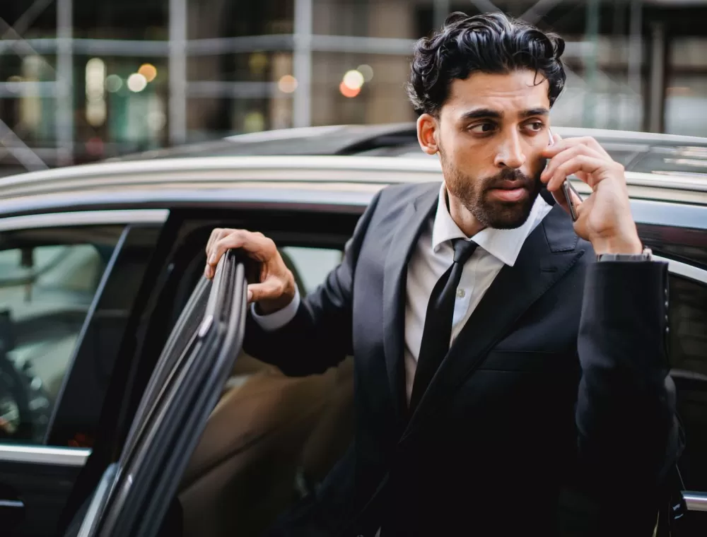 A salesperson taking a call on his phone as he steps out of a car