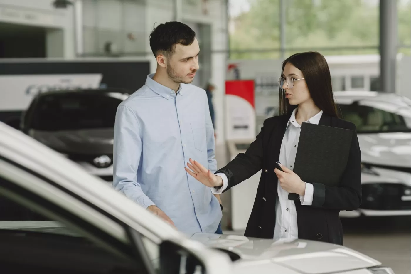 A salesperson guiding a customer around a new vehicle on the showroom floor